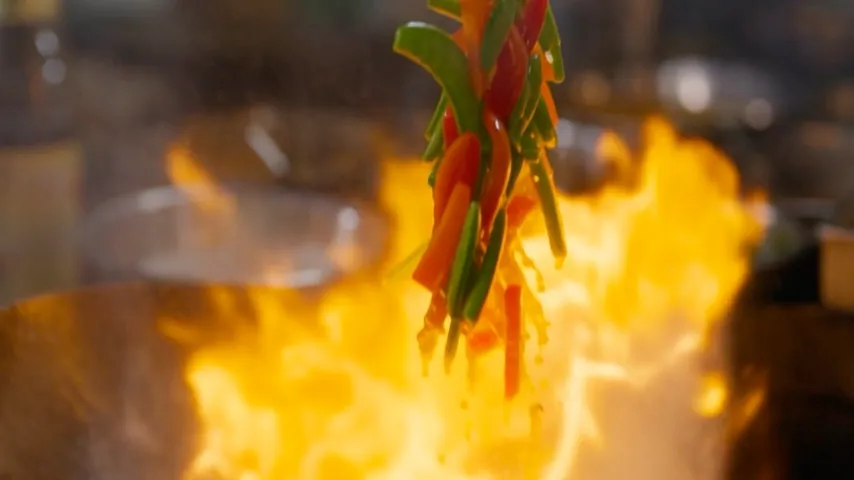 Original video frame at seven seconds: sliced vegetables rise above the flames in close-up